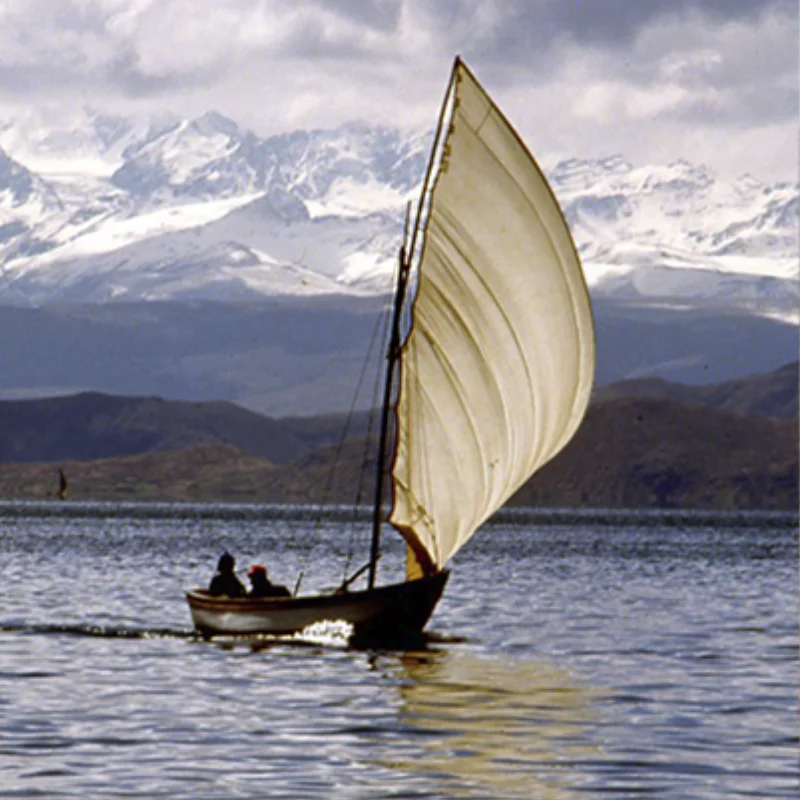 Velero navegando por una laguna del altiplano con la cordillera nevada al fondo.