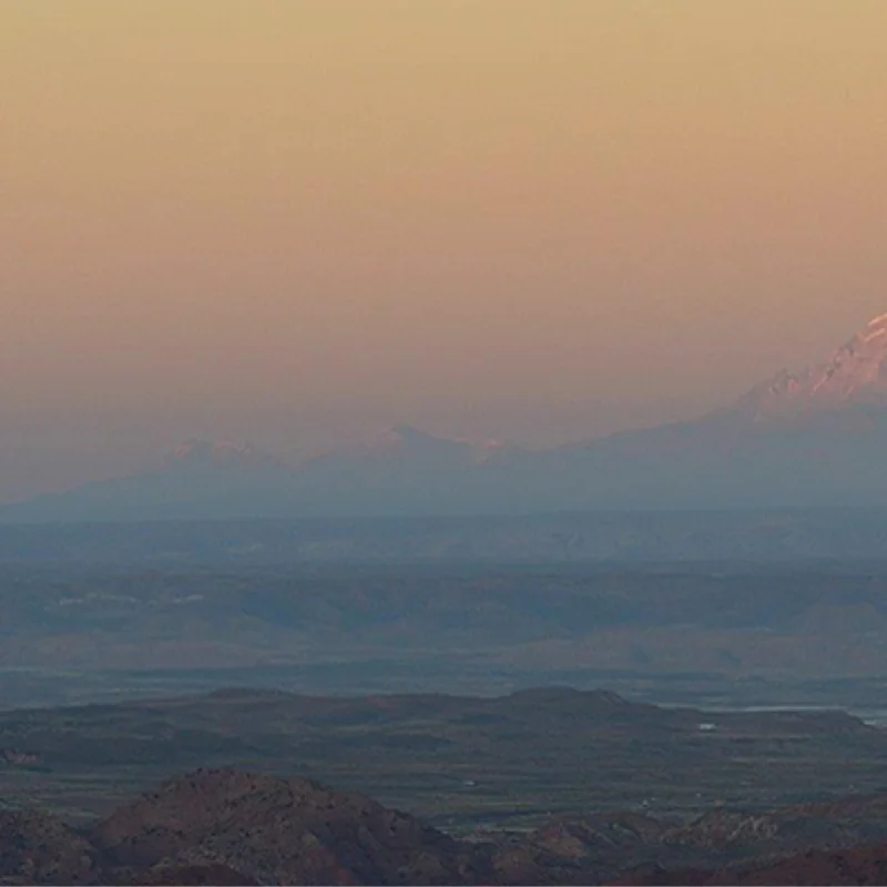 Paisaje del altiplano con montañas nevadas en el horizonte durante el atardecer.
